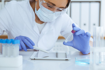 Close-up of professional female scientist in protective eyeglasses making experiment with reagents...