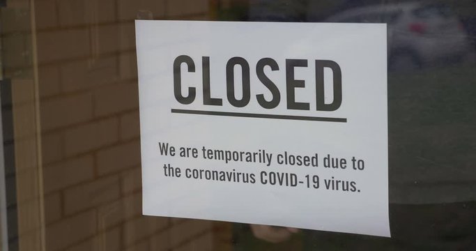 A business owner puts a CLOSED sign on the front door due to the coronavirus COVID19 pandemic.  	