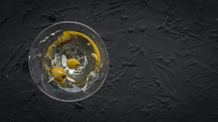Dirty martini with green olive in a cocktail glass on black concrete
