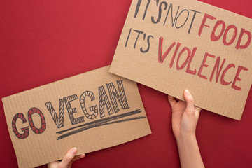 partial view of woman holding cardboard signs with go vegan and its not food its violence inscriptions on red background