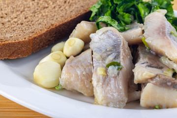 herring with brown bread, onions, garlic and parsley on the white plate