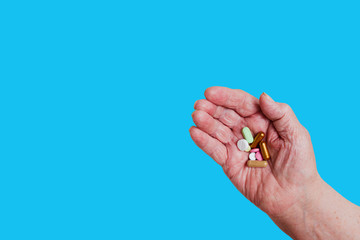 Many different pills in the hand of an elderly person. Isolated on blue background.