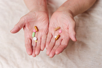 Many different pills in the hands of an elderly person.
