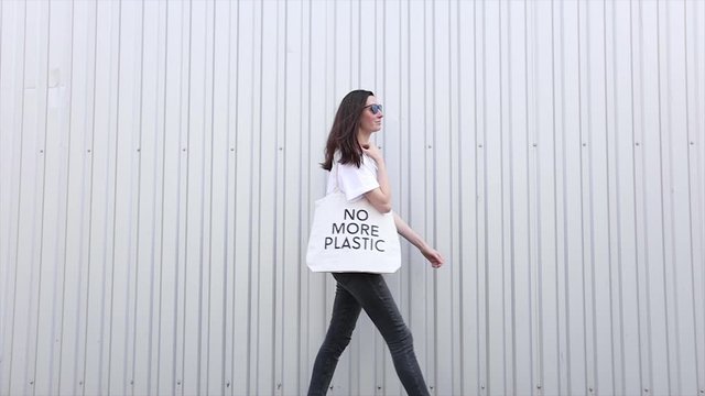 No more plastic eco concept of woman holding white textile eco bag against metal wall background. Ecology or environment protection concept. White eco bag for mock up.