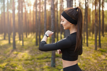 Woman running in the woods checking smartwatch. Natural light in forest. 