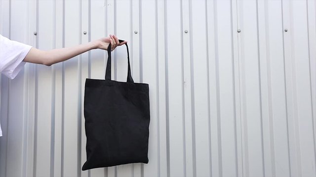 Young woman holding white textile eco bag againstwhite wall. Ecology or environment protection concept. White eco bag for mock up.