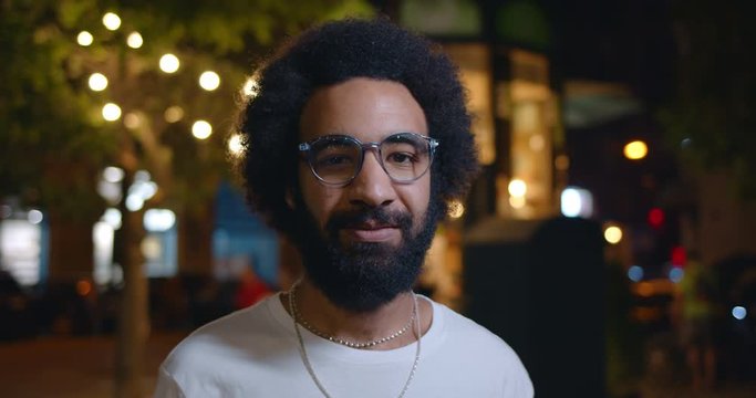 Portrait of handsome arab man in glasses looking to camera. Close up view of bearded man in 30s standing at street of night city. Concept of people and lifestyle.