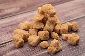 A pile of brown cane sugar lumps on a wooden background. Close up.