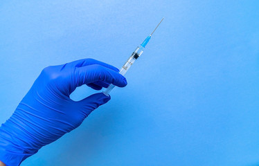 A syringe containing the coronavirus vaccine is held by a blue-gloved hand on a blue background in...