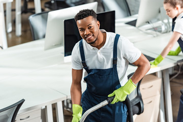 smiling african american cleaner looking at camera near young colleague