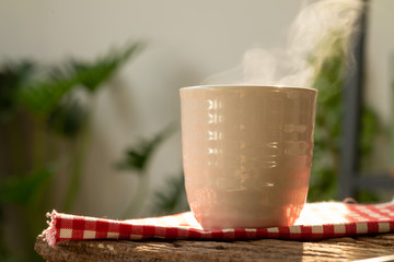 A cup of tea or hot water with hot steam placed on the table in the garden