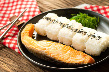 Grilled salmon with soy sauce with Japanese rice topped with black sesame seeds in a black plate on a wooden table