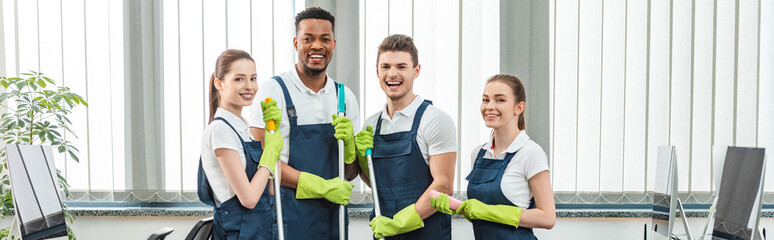 panoramic shot of cheerful multicultural team of cleaners looking at camera while standing in office