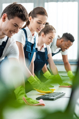 selective focus of young multicultural cleaners wiping desks with rags in office
