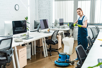 cheerful cleaner looking at camera while washing floor with cleaning machine