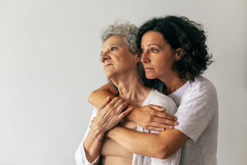 Pensive adult daughter hugging senior mother and looking away. Middle aged woman embracing elderly...