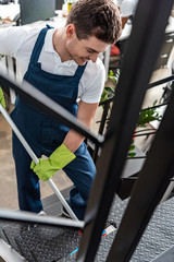 selective focus of smiling young cleaner washing stairs with mop