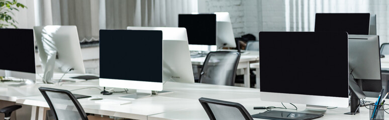 panoramic shot of open space office with computer monitors on white desks