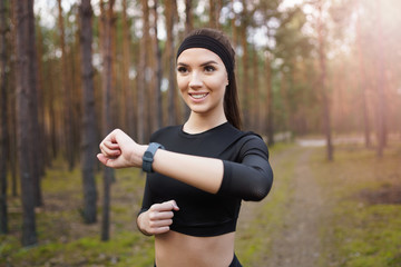 Woman running in the woods checking smartwatch. Natural light in forest. 