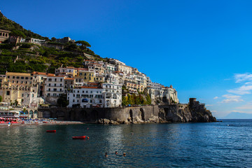 Fototapeta na wymiar View of the beach with its bathers from the town of Amalfi from the jetty with the sea, boats and colorful houses on the slopes of the Amalfi coast in the province of Salerno, Campania, Italy.
