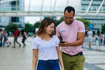 Smiling young couple looking at smartphone. Cheerful people talking and looking at phone during stroll. Technology concept