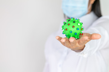 The hand of an Asian woman in a white doctor's outfit, holding a green ball with a virus-like , the idea of ​​dealing with the virus Covid 19.