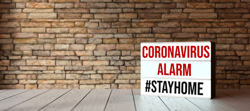 lightbox with text CORONAVIRUS ALARM #STAYHOME in front of a brick wall on wooden floor