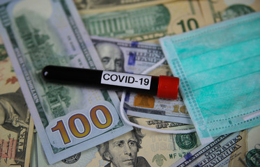 Corona virus covid-19 uncertain consequential costs concept symbol: closeup of isolated blood sample vial ans surgical protection face mask on us dollar paper money bank nots