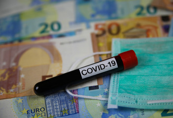 Corona virus uncertain consequential costs concept symbol: closeup of isolated blood sample vial on euro paper money bank notes und surgical mask