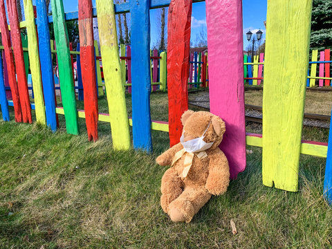 Teddy Bear in the medical mask under the colorful fence