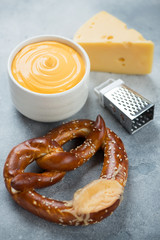 Close-up of german pretzel served with cheese dipping sauce, studio shot on a light-blue stone background