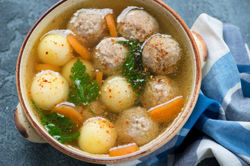 Close-up of soup with meatballs and potato balls served in a beige bowl, elevated view, studio shot