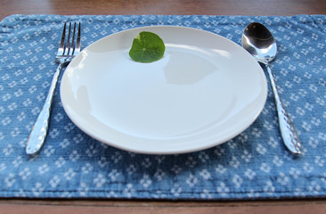 A small green leaves decorated on a white ceramic plate with spoon and fork on blue placemat.