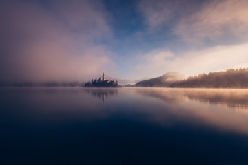 Fototapeta na wymiar Amazing view on a misty morning of lake Bled with St. Marys Church of the Assumption on the small island; Bled, Slovenia, Europe.