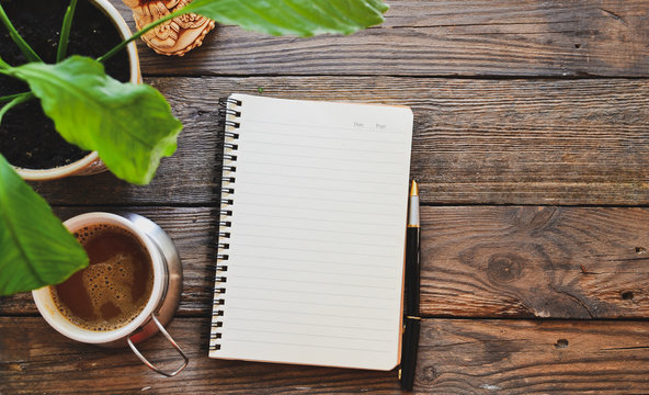 Notebook and coffee, flowerpot, notebook and pen, wooden background, top view. Work at home. Office accessories and office wooden table.