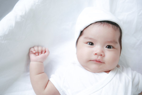 Portrait  of a newborn Asian child wearing a white dress on a white mattress