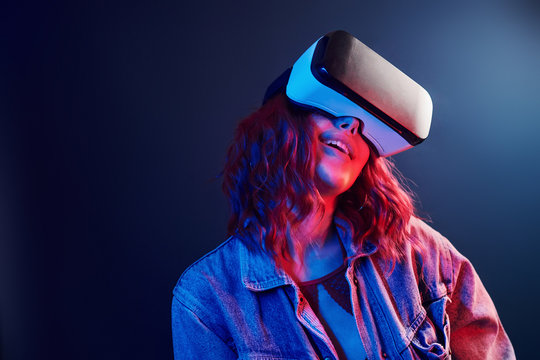 Facial expression of young girl with virtual reality glasses on head in red and blue neon in studio