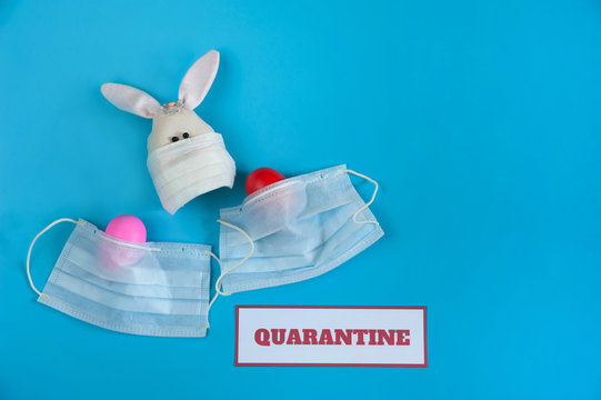 The concept of quarantine at Easter time. Easter Bunny and painted eggs in a medical mask, a message about quarantine on a light blue background. Free space.