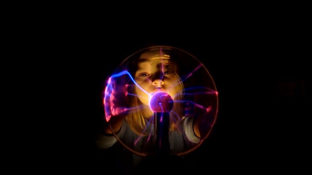 Pretty girl moves her fingers on the surface of the plasma tesla ball and watches for changes in condition