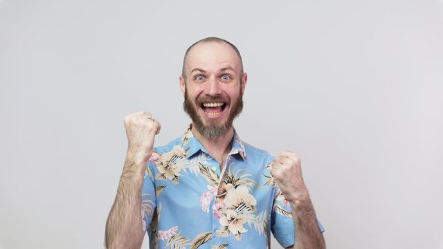 Happy man wearing hawaiian shirt celebrating a victory over white background. Emotions of success, triumph, victory, winning and celebration.