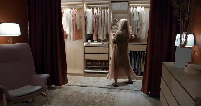 Beautiful aged woman thinking what to dress in walk-in closet