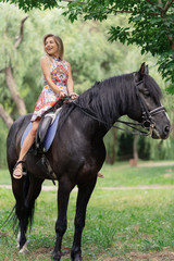 Fototapeta premium Young woman in a bright colorful dress riding a black horse