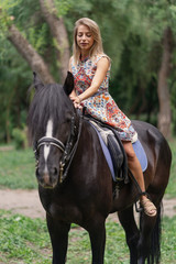 Young woman in a bright colorful dress riding a black horse