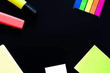 Frame of a desk with post its and a markers on black background