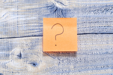 Post it on wooden background with a question mark