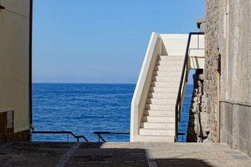 Fototapeta na wymiar White stairs between building in Southern Europe near the ocean. The entrance to the apartment on a coast at vacation.
