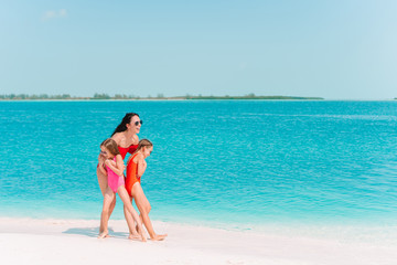 Fototapeta na wymiar Adorable little girls and young mother on tropical white beach
