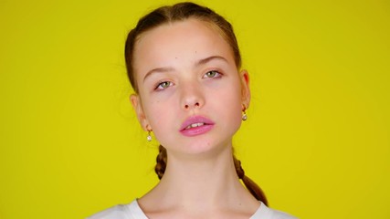 Teenage girl in a white T-shirt chews gum and inflates a bubble. Yellow background with copy space. Teenager emotions. 4k footage