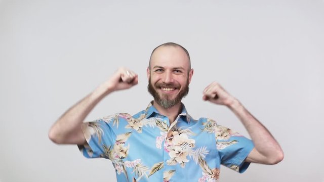 Happy man wearing hawaiian shirt celebrating a victory over white background, slow motion. Emotions of success, triumph, victory, winning and celebration.