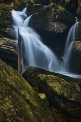 Waterfall on the black brook in the middle of spring forest. Long exposure silk flows of water.
